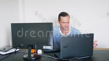 一个男人<strong>坐在</strong>家里的办公桌<strong>前</strong>，在家里的<strong>电脑</strong>和笔记本<strong>电脑</strong>里工作。
